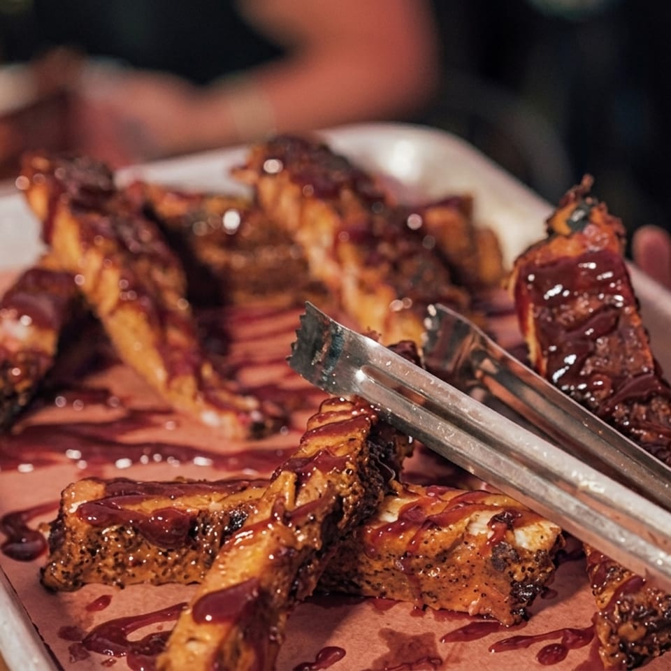 A tray of BBQ ribs with sauce, being served with tongs.