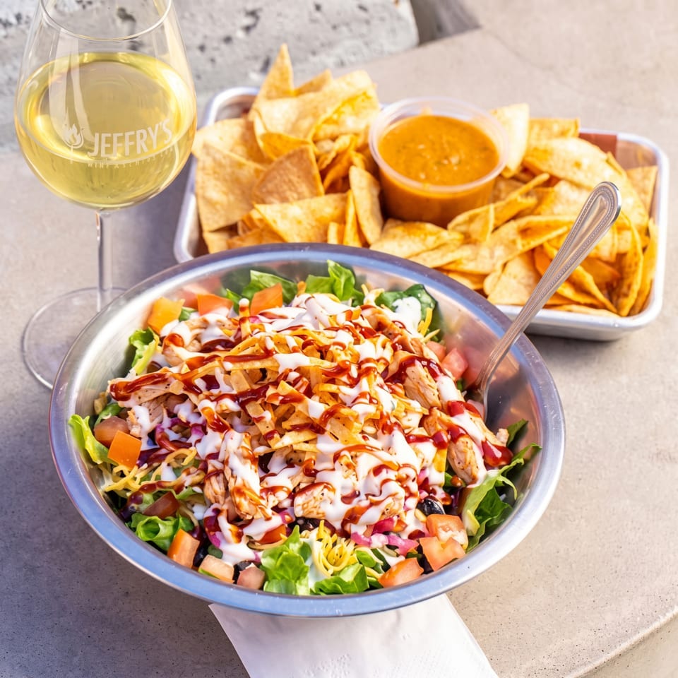 Loaded chicken salad with vegetables, crispy tortilla strips, creamy and barbecue sauces, tortilla chips, salsa, and white wine.